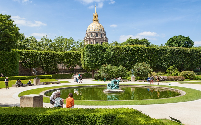 Rodin Museum garden with sculptures and pond, Paris, featuring the golden dome of Les Invalides.