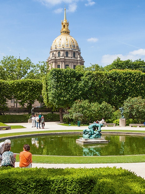 Rodin Museum garden with sculptures and pond, Paris, featuring the golden dome of Les Invalides.