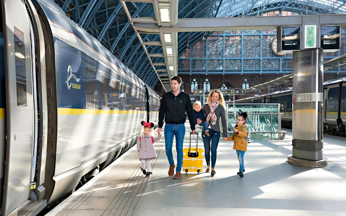 Family walking at St Pancras International station beside Eurostar train to Paris.