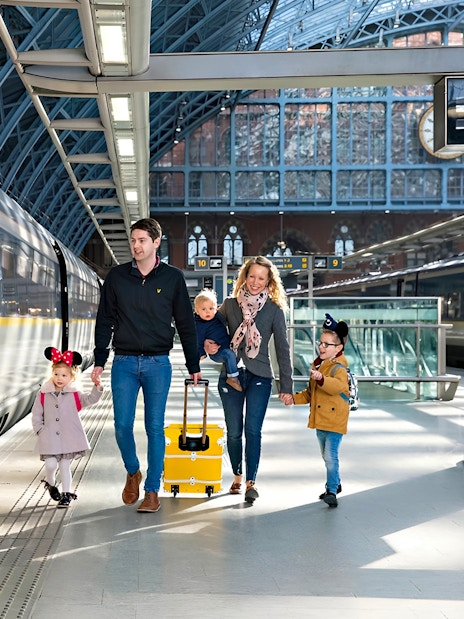 Family walking at St Pancras International station beside Eurostar train to Paris.