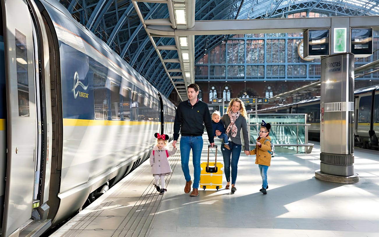 Family walking at St Pancras International station beside Eurostar train to Paris.