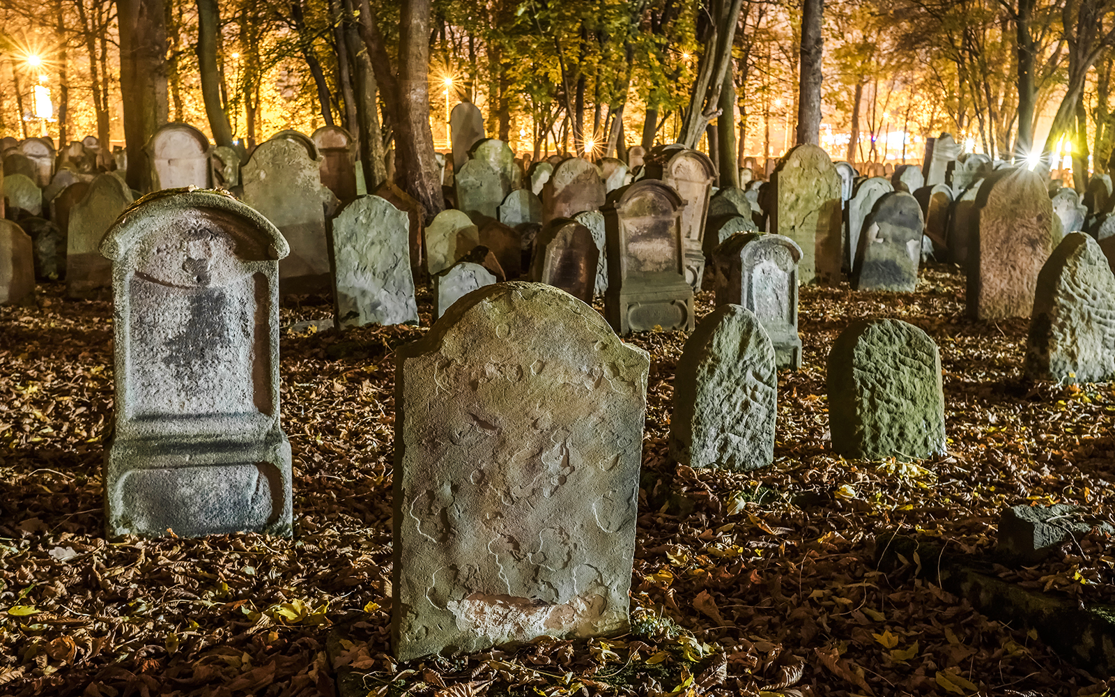 Tombstones in a dimly lit old cemetery surrounded by trees at night.