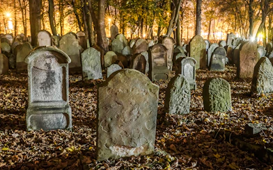 Tombstones in a dimly lit old cemetery surrounded by trees at night.