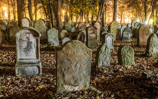 Tombstones in a dimly lit old cemetery surrounded by trees at night.