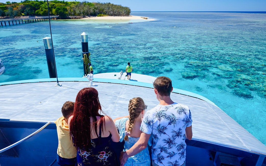 Tourists on a boat approaching Fitzroy Island, with clear blue waters and coral reefs visible.