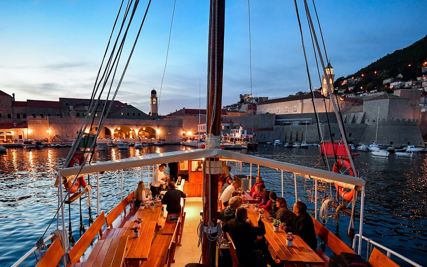 Dinner cruise in Dubrovnik harbor with guests dining on a boat at sunset.