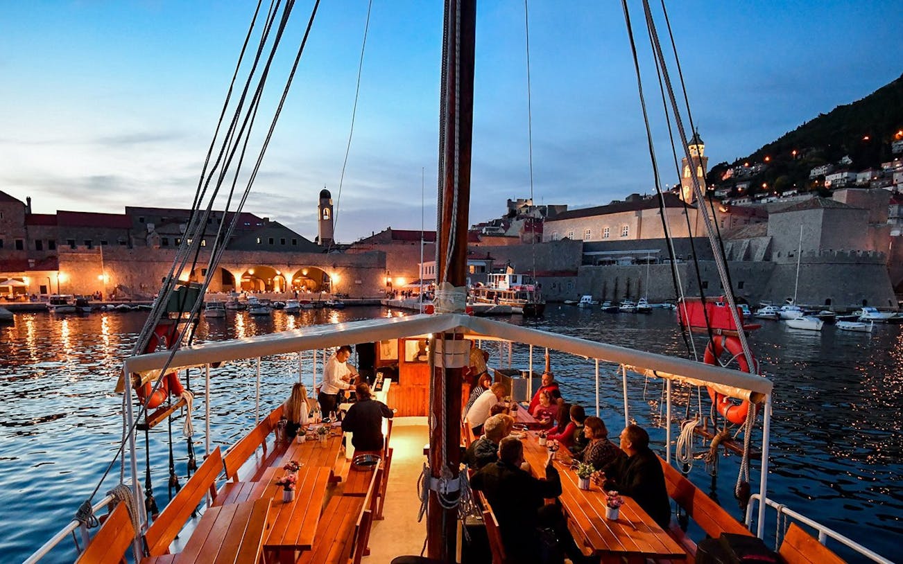 Dinner cruise in Dubrovnik harbor with guests dining on a boat at sunset.