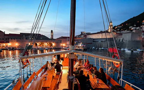 Dinner cruise in Dubrovnik harbor with guests dining on a boat at sunset.