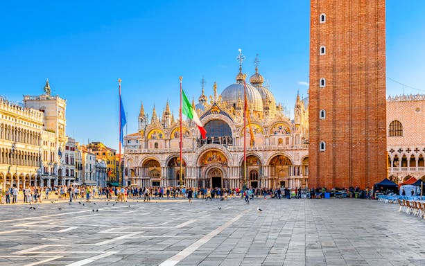St. Mark's Basilica and Campanile in Venice, Italy, with tourists in the square.