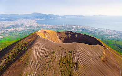 Aerial view of Mount Vesuvius crater with Naples and coastline in the background.