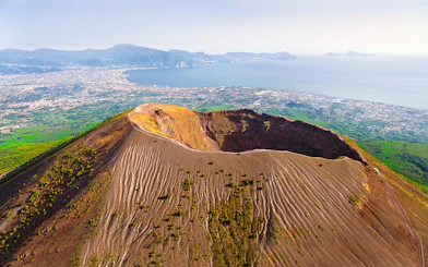 Aerial view of Mount Vesuvius crater with Naples and coastline in the background.