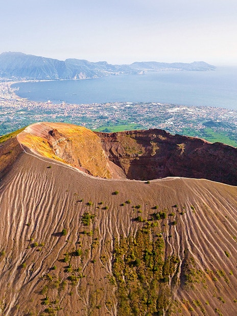 Aerial view of Mount Vesuvius crater with Naples and coastline in the background.