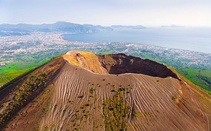Aerial view of Mount Vesuvius crater with Naples and coastline in the background.