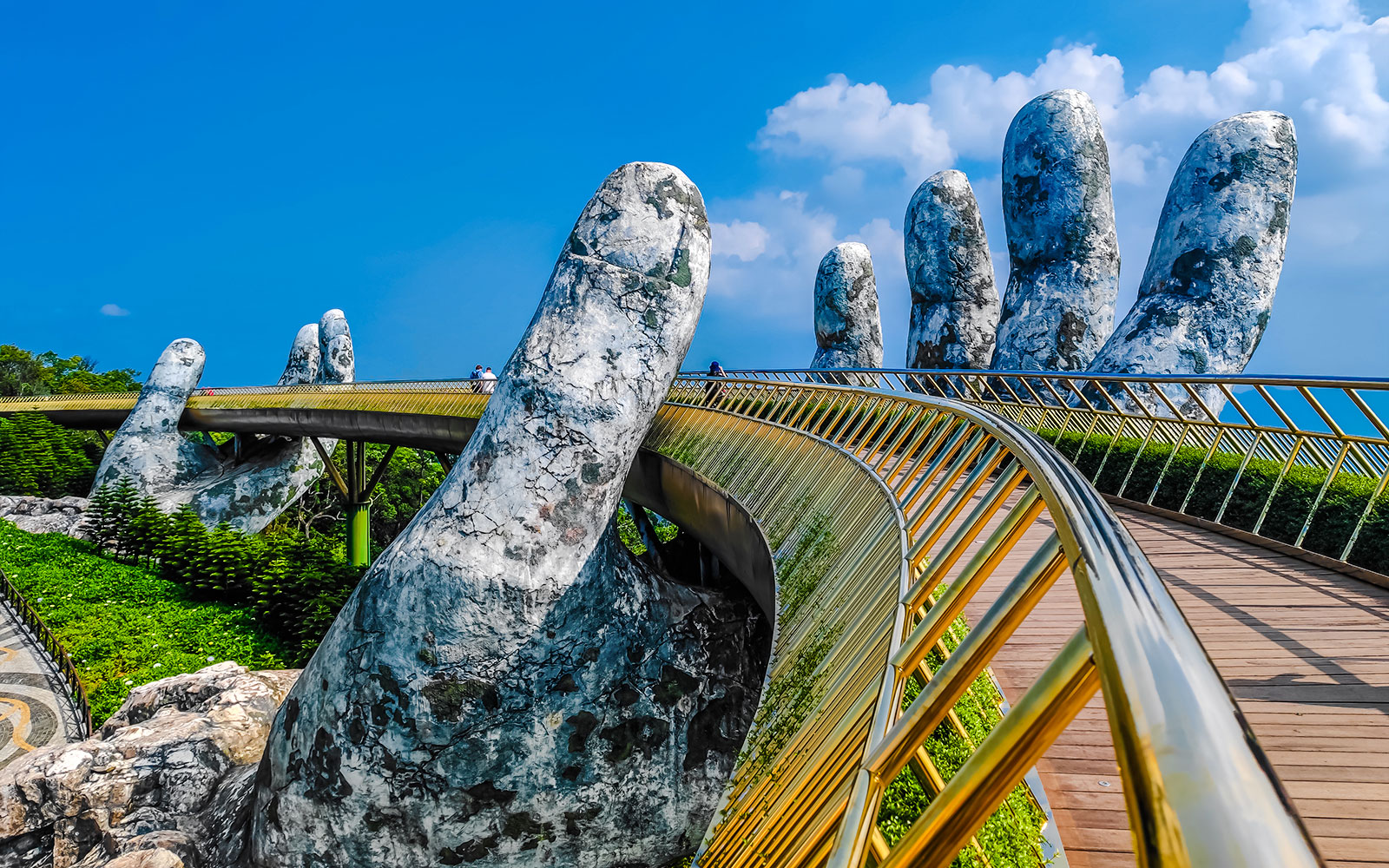 Golden Bridge in Ba Na Hills supported by giant stone hands against a clear blue sky.