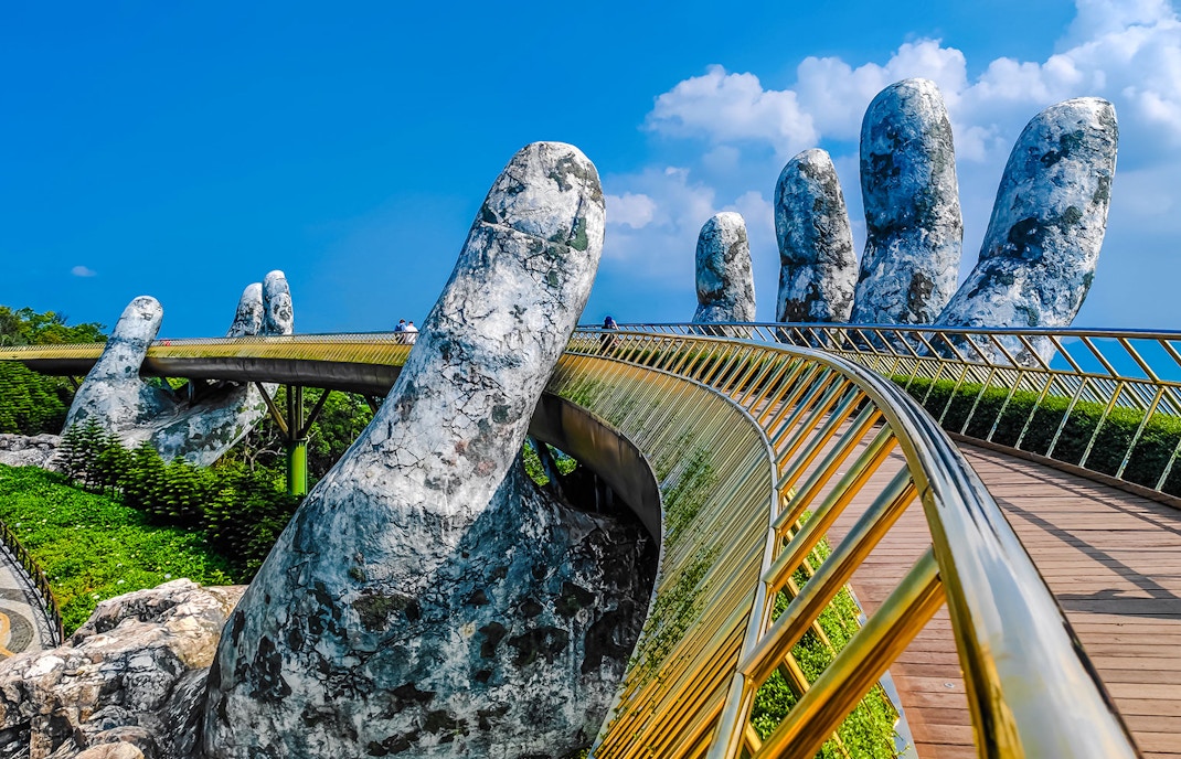 Golden Bridge in Ba Na Hills supported by giant stone hands against a clear blue sky.