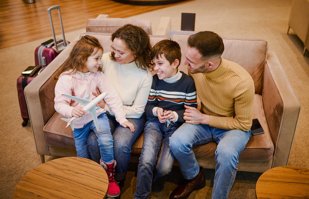 Family sitting together in airport lounge with luggage nearby.