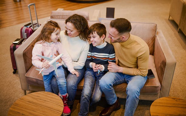 Family sitting together in airport lounge with luggage nearby.