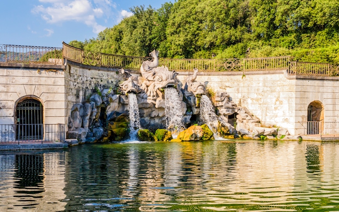 Three dolphins fountain at Royal Palace of Caserta with water flowing into a pond.