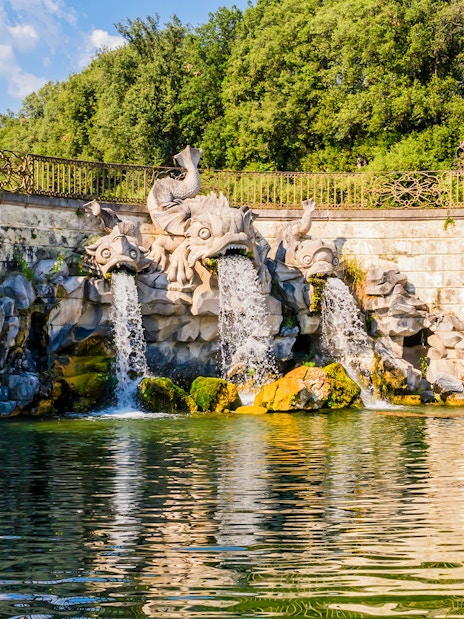 Three dolphins fountain at Royal Palace of Caserta with water flowing into a pond.