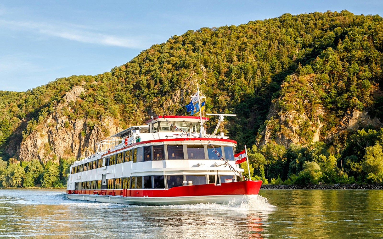 Cruise ship on the Danube River with forested hills in Vienna, Austria.