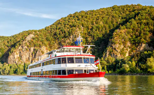 Cruise ship on the Danube River with forested hills in Vienna, Austria.