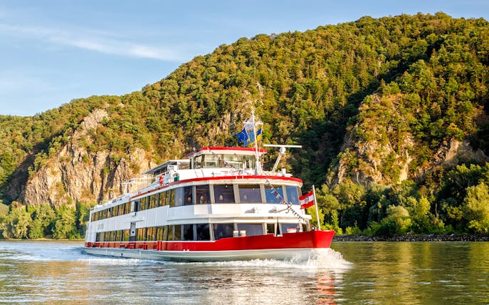 Cruise ship on the Danube River with forested hills in Vienna, Austria.