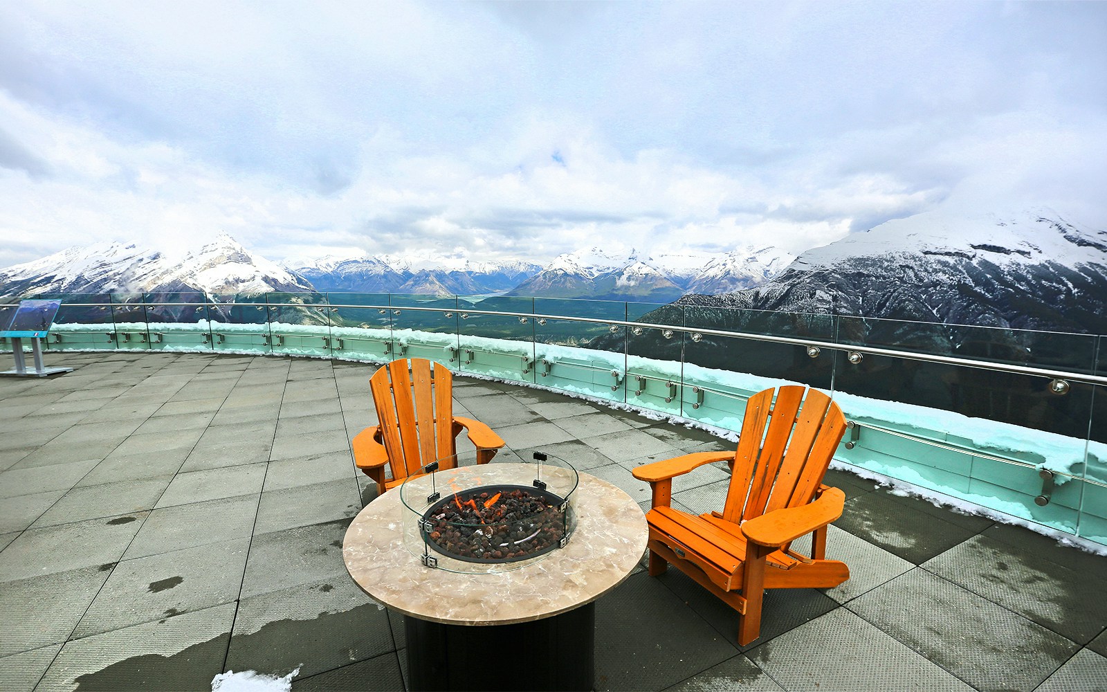 Banff observation deck with chairs and fire pit overlooking snowy mountains, Canada.