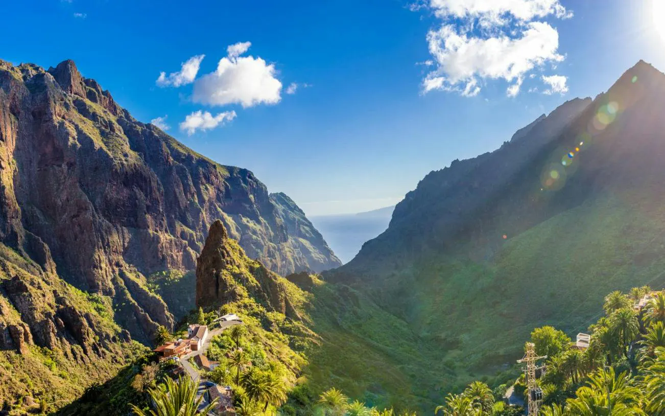 Masca Village nestled in lush green mountains, Tenerife, with ocean view in the distance.