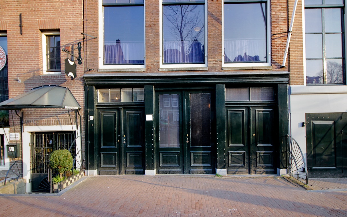 Exterior of the Anne Frank House in Amsterdam with black doors and brick facade.