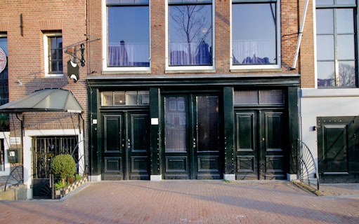 Exterior of the Anne Frank House in Amsterdam with black doors and brick facade.