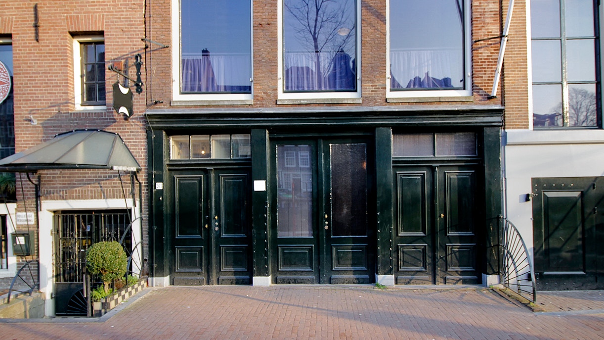 Exterior of the Anne Frank House in Amsterdam with black doors and brick facade.
