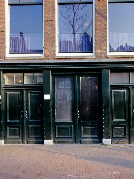 Exterior of the Anne Frank House in Amsterdam with black doors and brick facade.