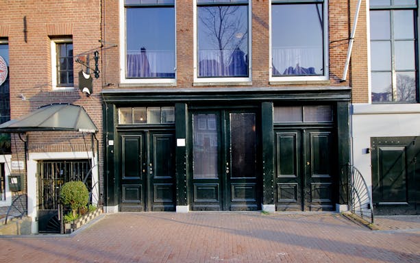Exterior of the Anne Frank House in Amsterdam with black doors and brick facade.
