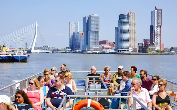 Sightseeing cruise passengers with Rotterdam skyline and Erasmus Bridge in background.