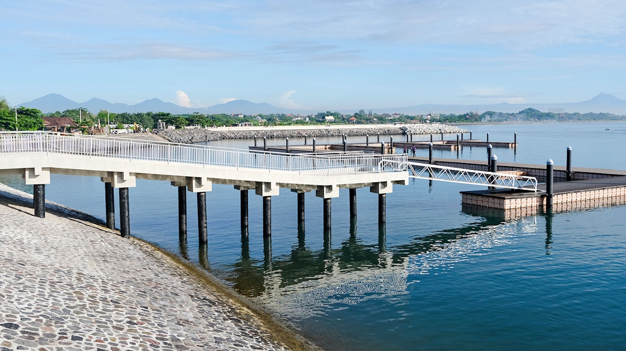 Sanur Harbor pier with clear water and distant mountains in Bali, Indonesia.