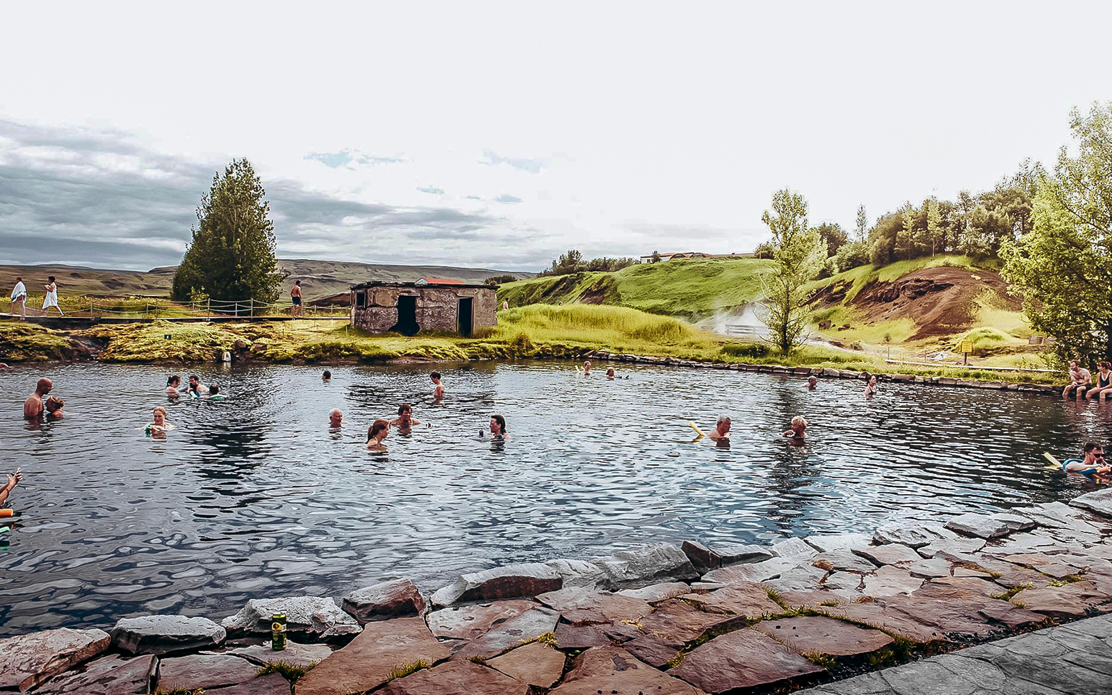 Guests enjoying a swim in Iceland's Secret Lagoon surrounded by lush greenery.
