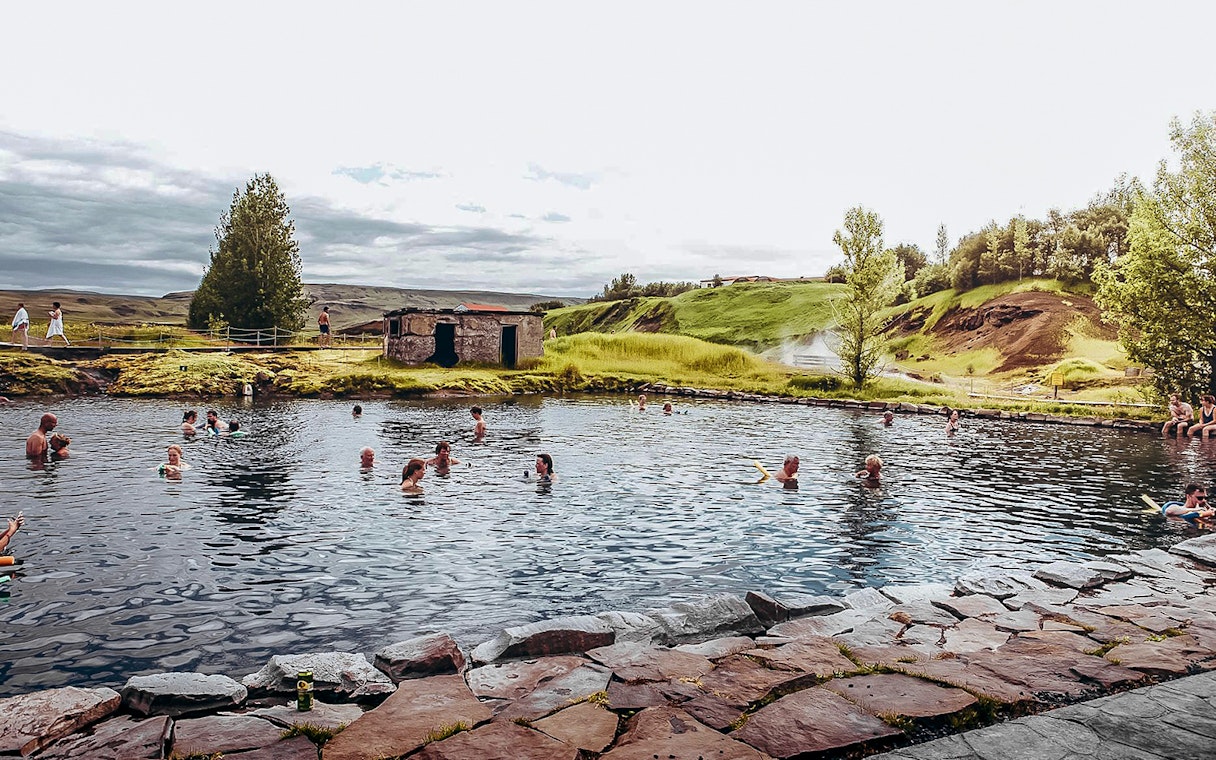 Guests enjoying a swim in Iceland's Secret Lagoon surrounded by lush greenery.
