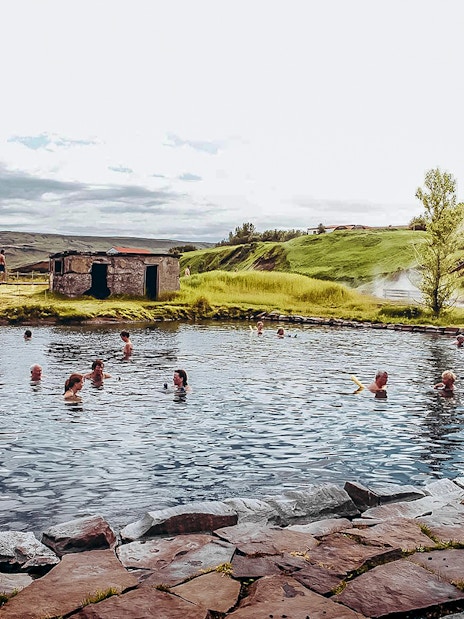 Guests enjoying a swim in Iceland's Secret Lagoon surrounded by lush greenery.