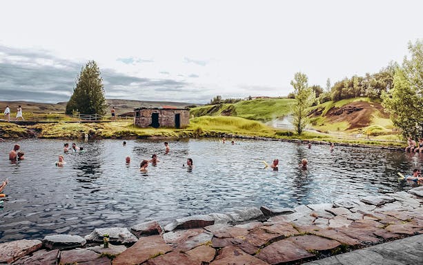 Guests enjoying a swim in Iceland's Secret Lagoon surrounded by lush greenery.