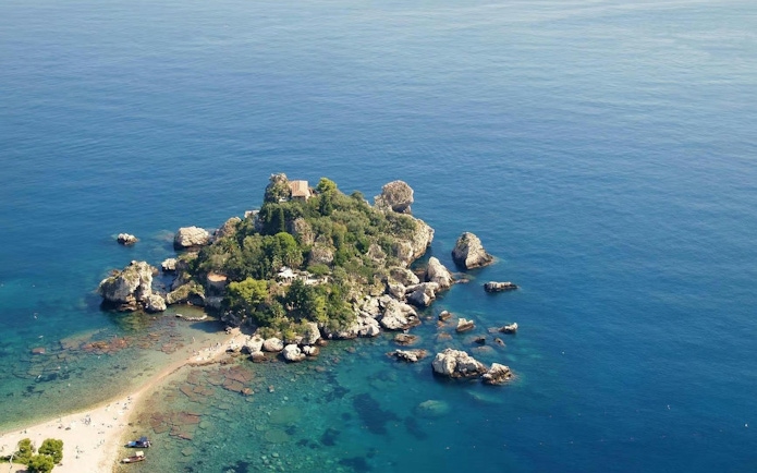 Aerial view of Isola Bella, Sicily, surrounded by clear blue sea and rocky coastline.