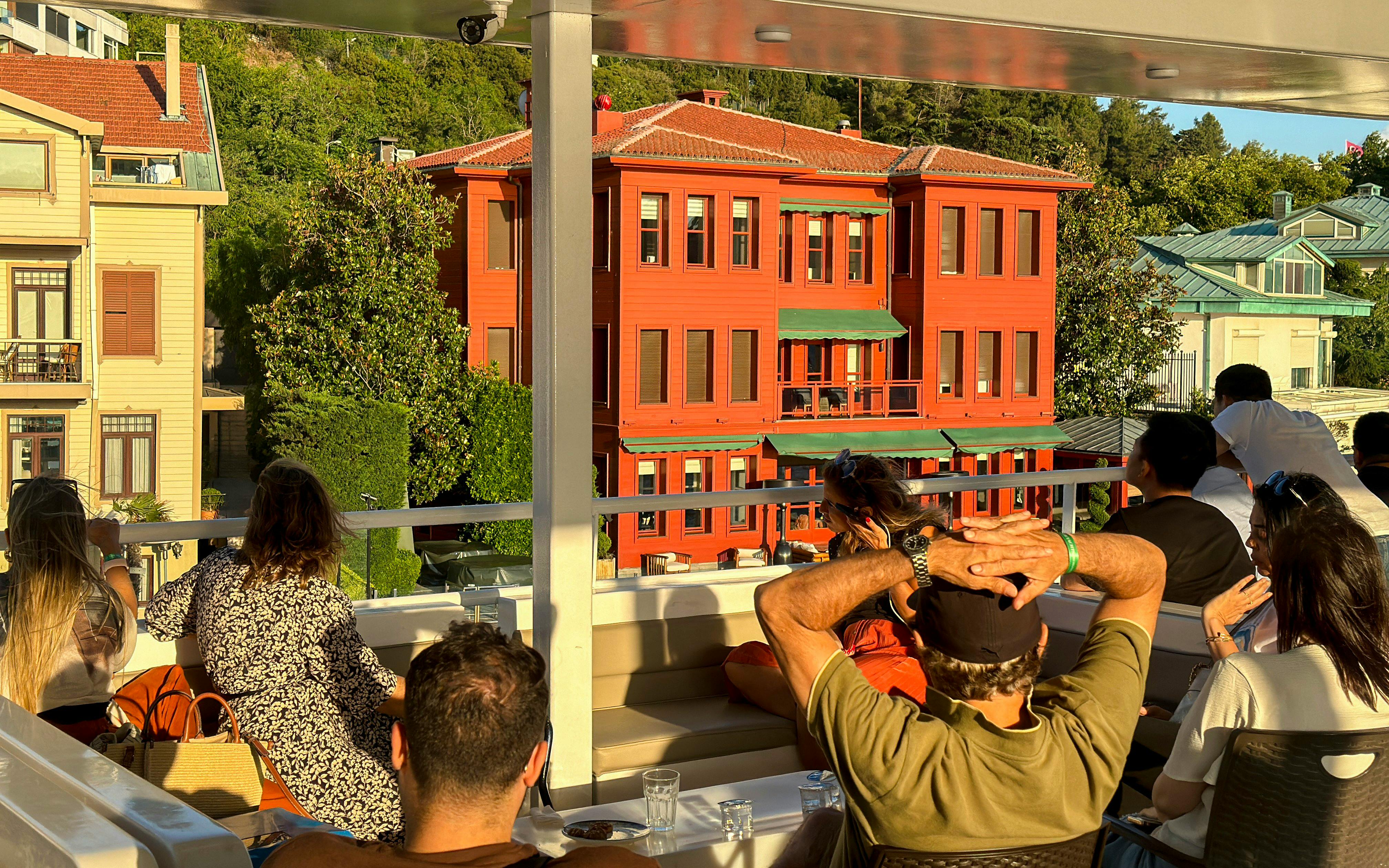Tourists on a Bosphorus cruise viewing historic waterfront mansions during sunset.