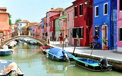 Colorful houses along Burano canals with boats and a footbridge.