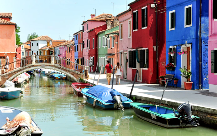 Colorful houses along Burano canals with boats and a footbridge.