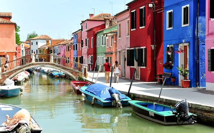 Colorful houses along Burano canals with boats and a footbridge.