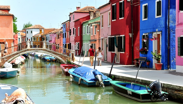 Colorful houses lining the Burano canals in Venice, Italy, with boats docked along the waterway.