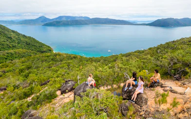 Tourists sitting on rocks overlooking ocean and forest on Fitzroy Island trail.