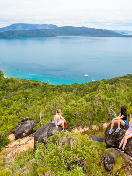 Tourists sitting on rocks overlooking ocean and forest on Fitzroy Island trail.