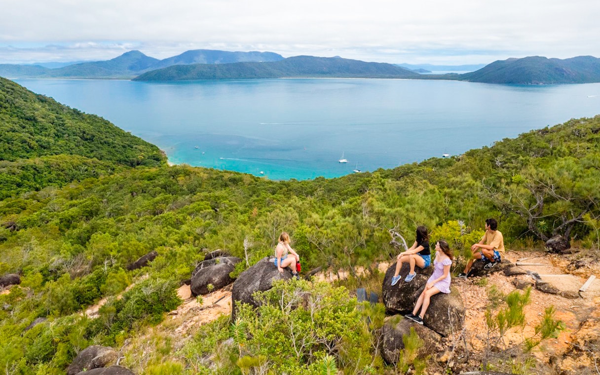 Tourists sitting on rocks overlooking ocean and forest on Fitzroy Island trail.