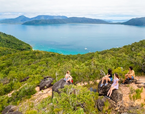 Tourists sitting on rocks overlooking ocean and forest on Fitzroy Island trail.