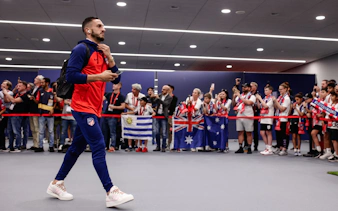 Atlético de Madrid player arrives, greeted by fans with flags and team scarves.